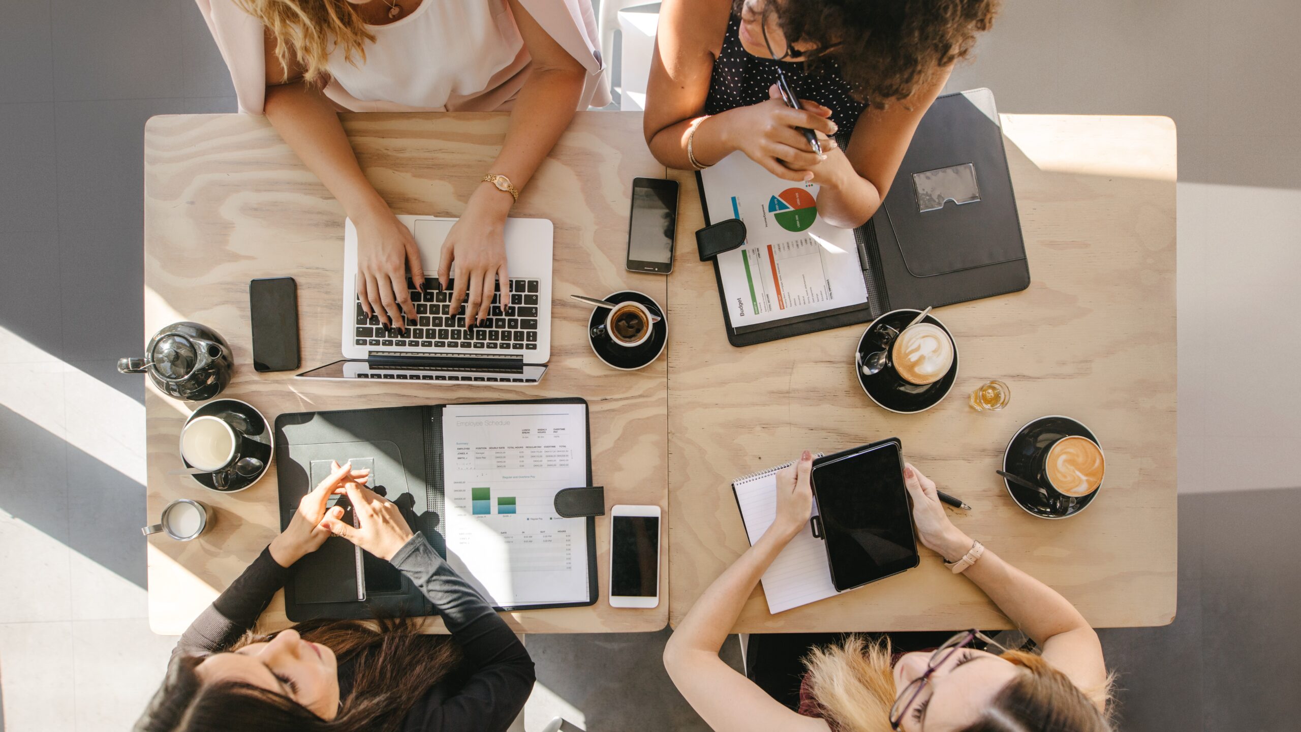 A marketing team sits around a table with laptops, mobile phones, and graphs